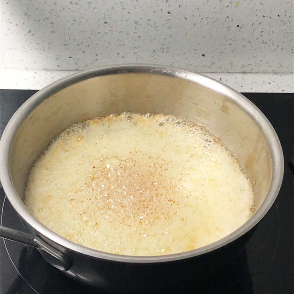 Foaming butter in saucepan with brown flecks on the surface of the foam, indicating brown butter is done.