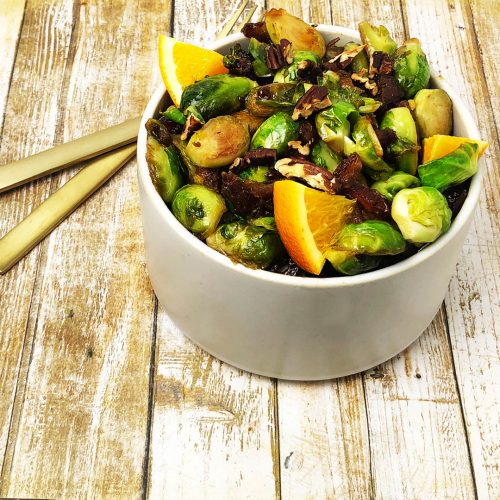 Cream coloured bowl filled with pan-fried brussell sprouts with orange, dates, and pecans