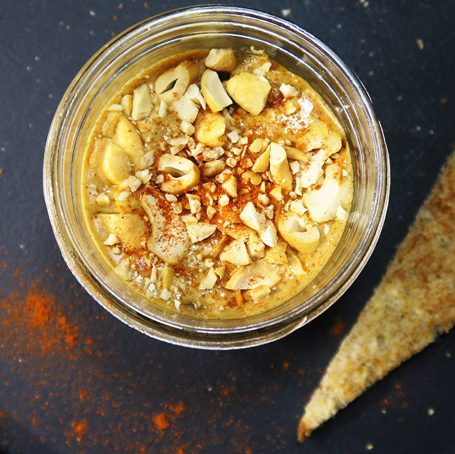 Top down view of spicy cashew butter in a glass jar against a dark background.