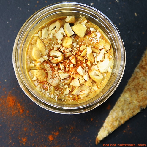 Top-down view of spicy cashew butter in a glass jar, against a dark background.