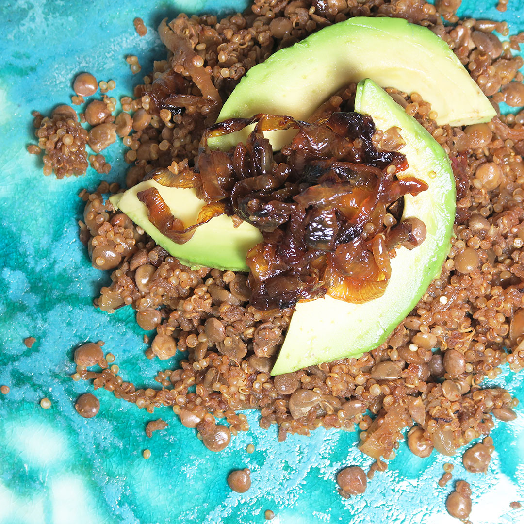 Top down view of Quinoa Mujadara, topped with caramelized onions and avocado, on a blue plate