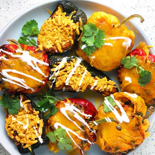 A colourful array of stuffed peppers, green, yellow, and red, topped with cheese, sour cream, and cilantro. From the recipe: Mexican Stuffed Pepper Three Ways - Vegan, Vegetarian, Omnivore