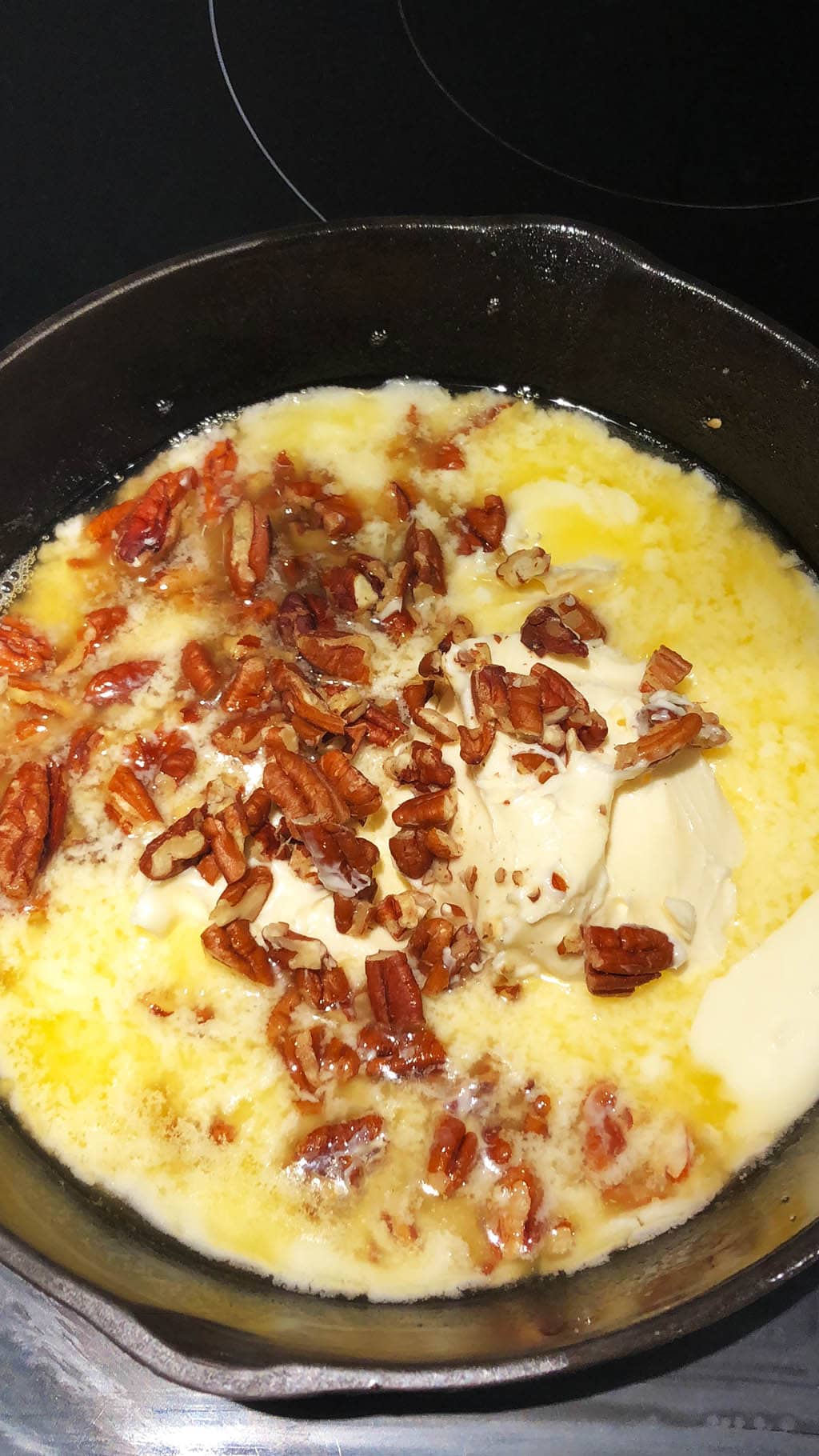 Melted margarine and pecans in a cast iron pan, making vegan brown butter