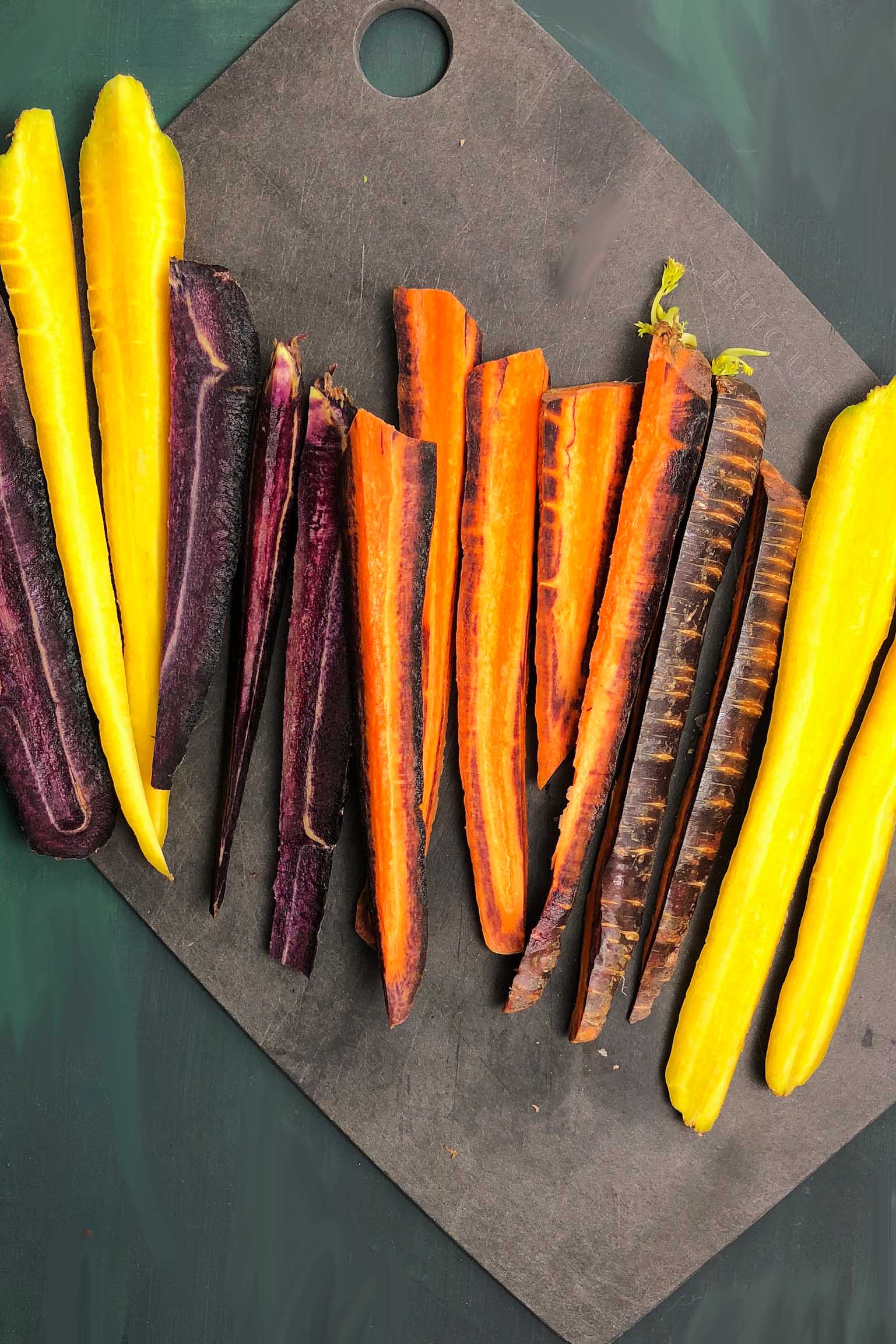 Sliced rainbow carrots on a cutting board. Carrots are yellow, orange, and purple.