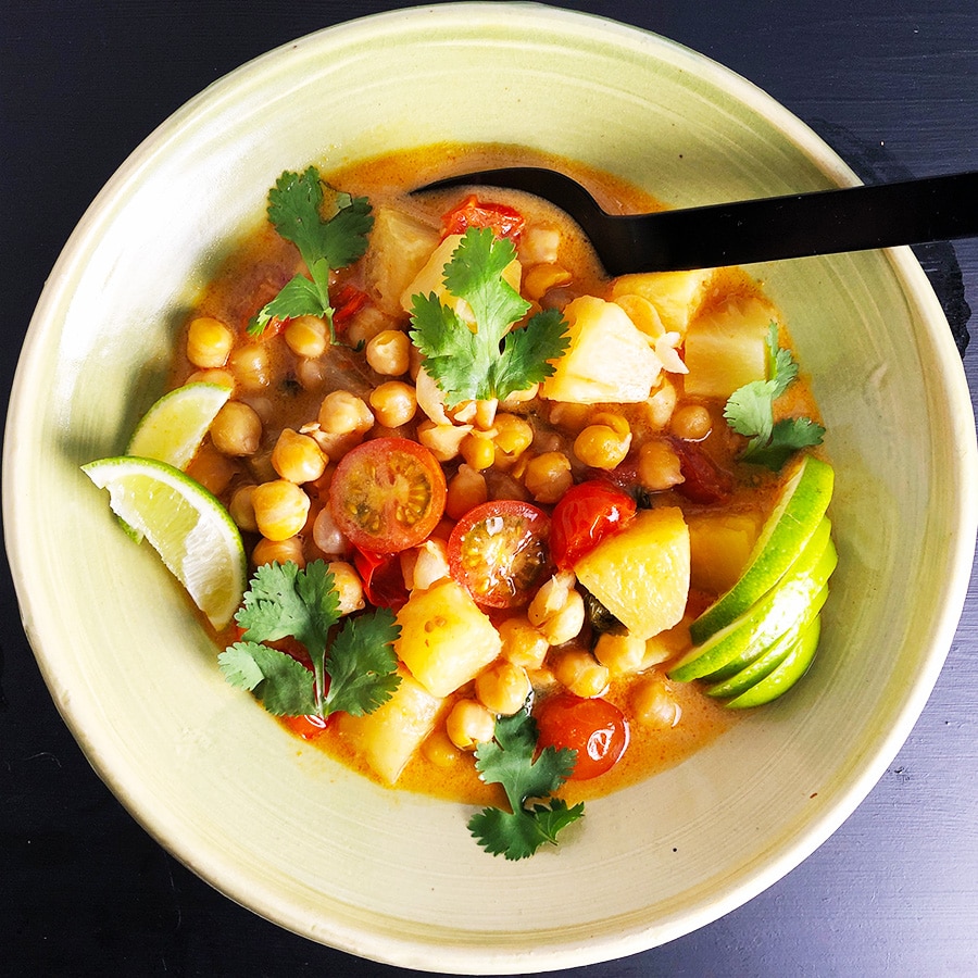 A topdown view of a bowl of Thai Chickpea Curry, containing red curry paste, coconut milk, chickpeas, tomatoes, pineapple, and seasonings.