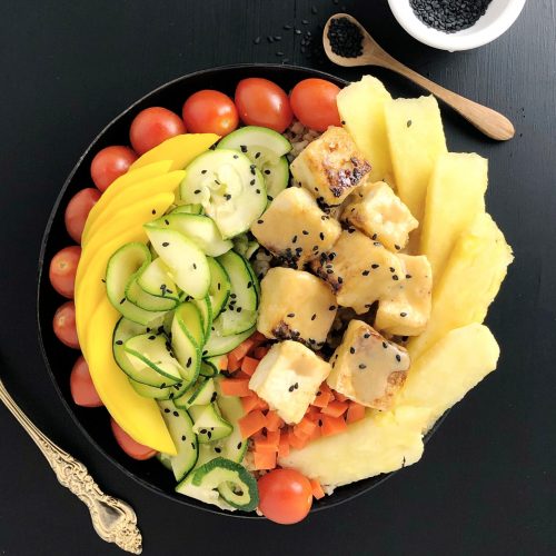 Top down view of Buddha Bowl with Pineapple Brown Butter Teriyaki Sauce on Salty Crispy Tofu, with cherry tomatoes, mango, raw zucchini, carrots, and pineapple.