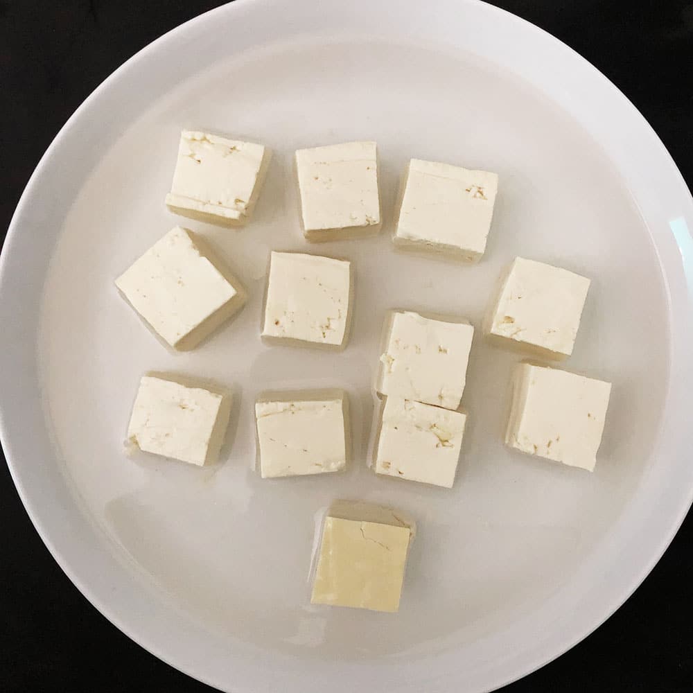 Top-down view of cubed tofu in a shallow white plate, topped with boiling salt water