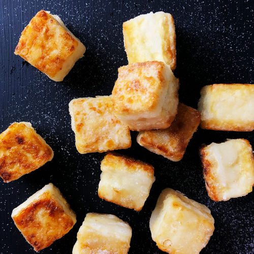 Cubes of Salty Crispy Tofu, sprinkled with salt, all against a black background