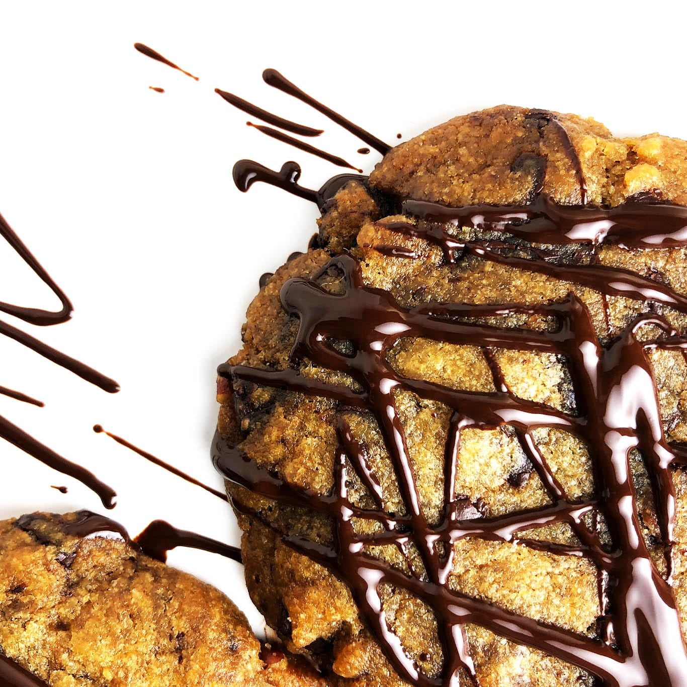 Close up, top-down shot of vegan brown butter chocolate chip cookies, drizzled with dark chocolate, on a white plate
