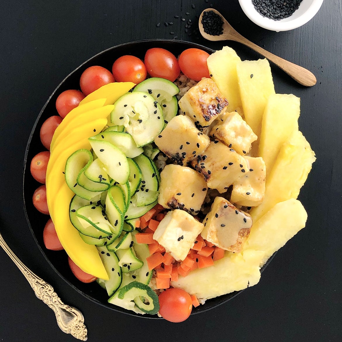 Top down view of Buddha Bowl with cherry tomatoes, mango slices, zucchini spirals, carrots, Salty Crispy Tofu topped with Pineapple Brown Butter Teriyaki Sauce, and fresh pineapple.
