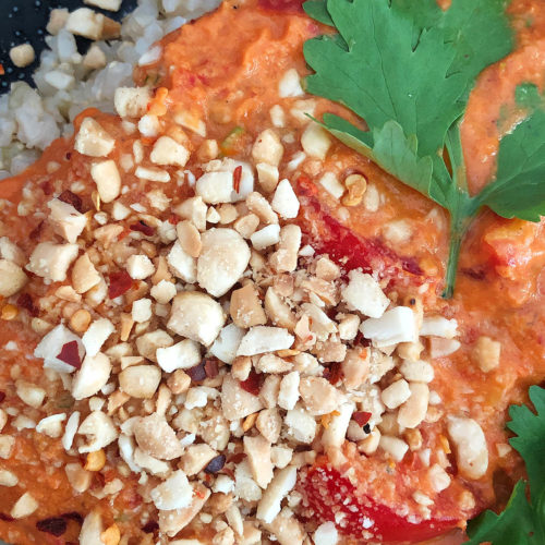 Top-down view of Spicy Tomato Peanut Sauce on brown rice, garnished with chopped peanuts and cilantro