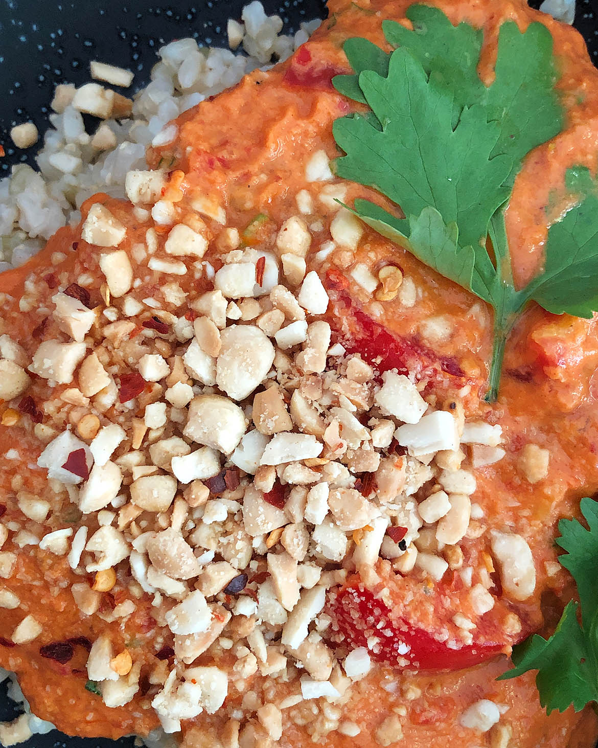 Top-down view of Spicy Tomato Peanut Sauce on brown rice, garnished with chopped peanuts and cilantro