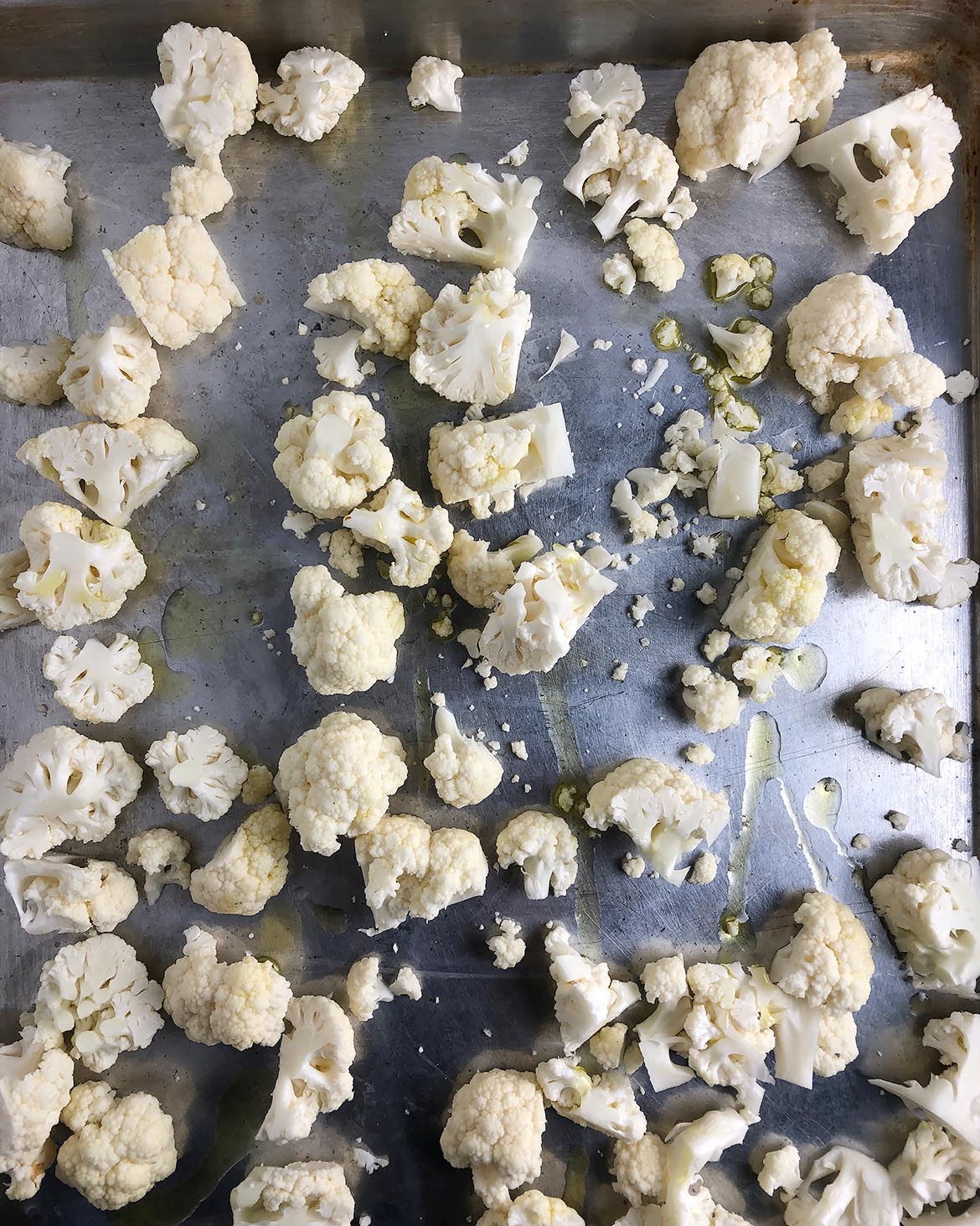 Topdown view of chopped cauliflower on a roasting pan, drizzled with olive oil