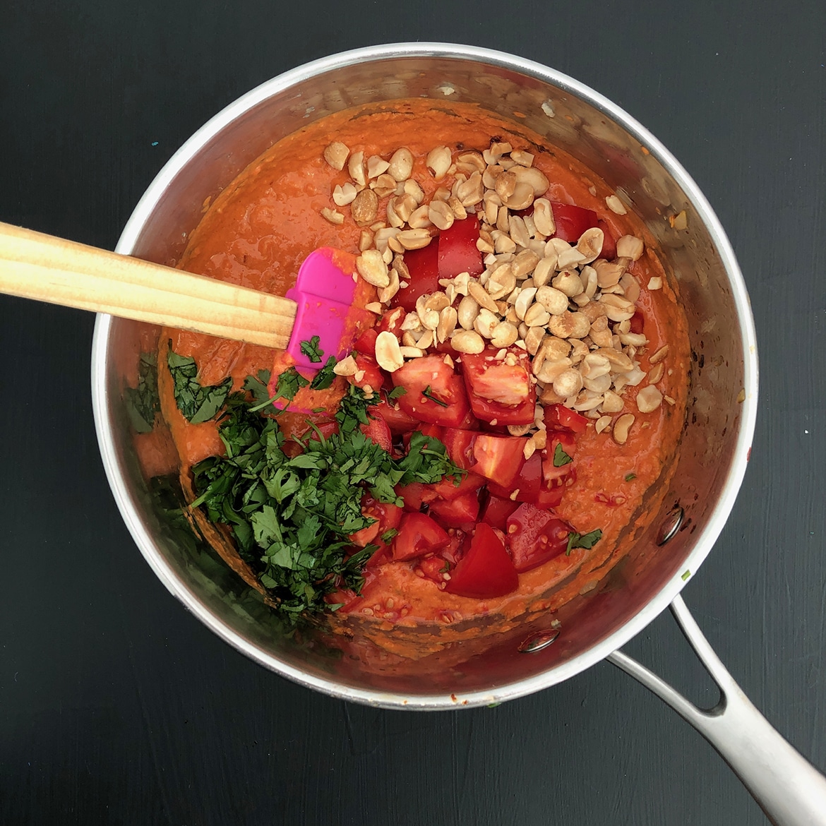 Top-down view of tomatoes, peanuts, and cilantro added to Spicy Tomato Peanut mixture. 