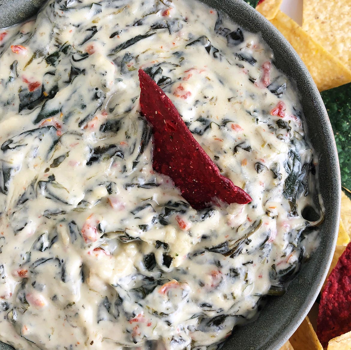 Top-down, close up view of Hot Spinach Dip with a red corn chip dipped in it