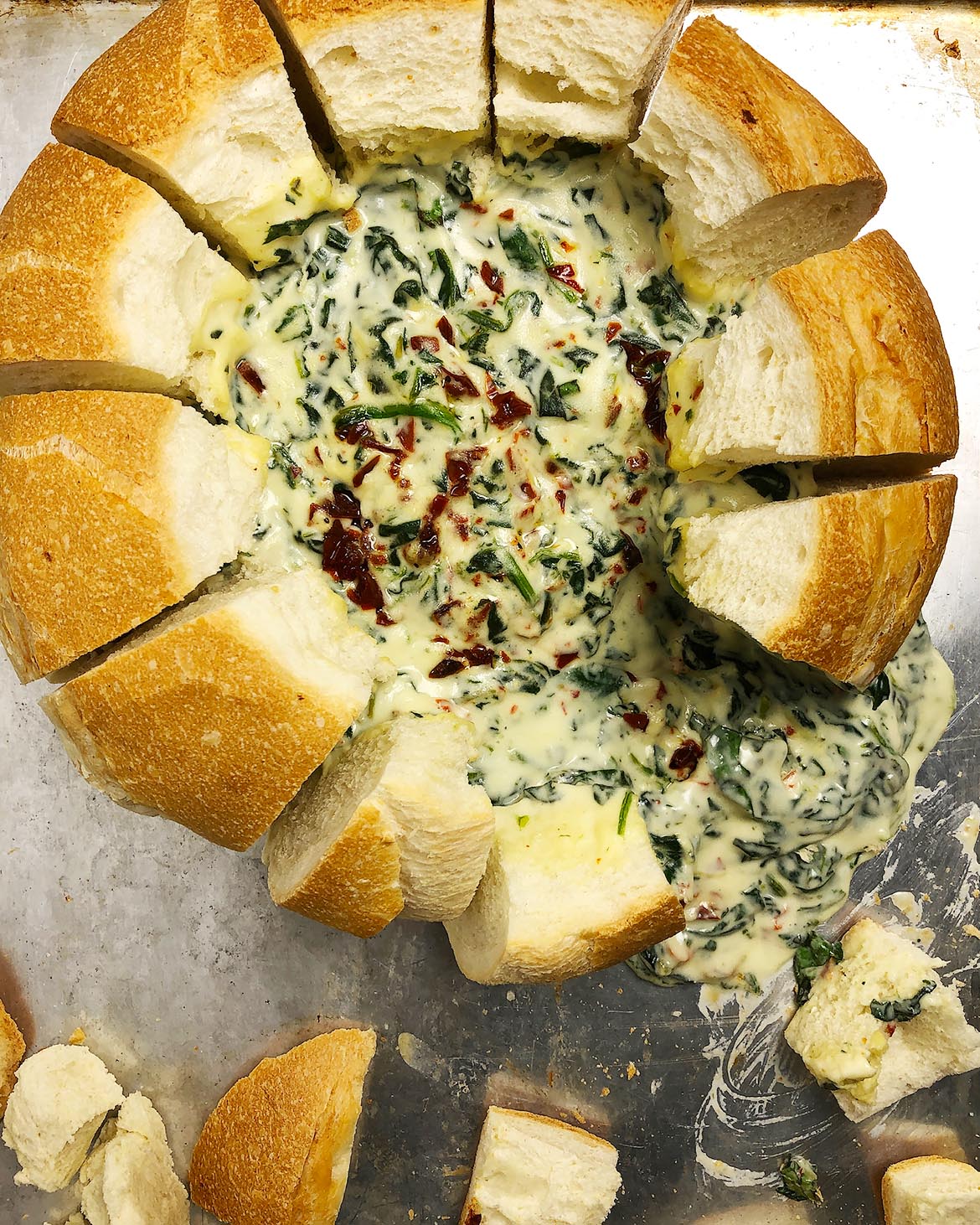 Top-down view of spinach dip in bread bowl, with cubes of bread pulled out of bowl