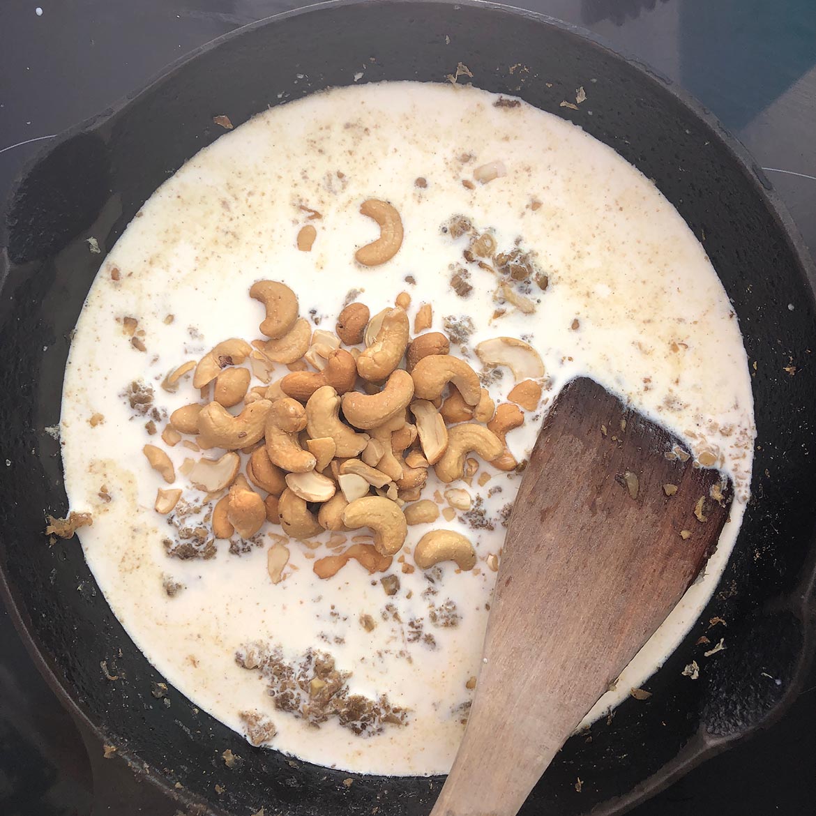 Top-down view of coconut milk and cashews added to the fried onions and spice mixture. Making Indian-Inspired Cashew Sauce. 
