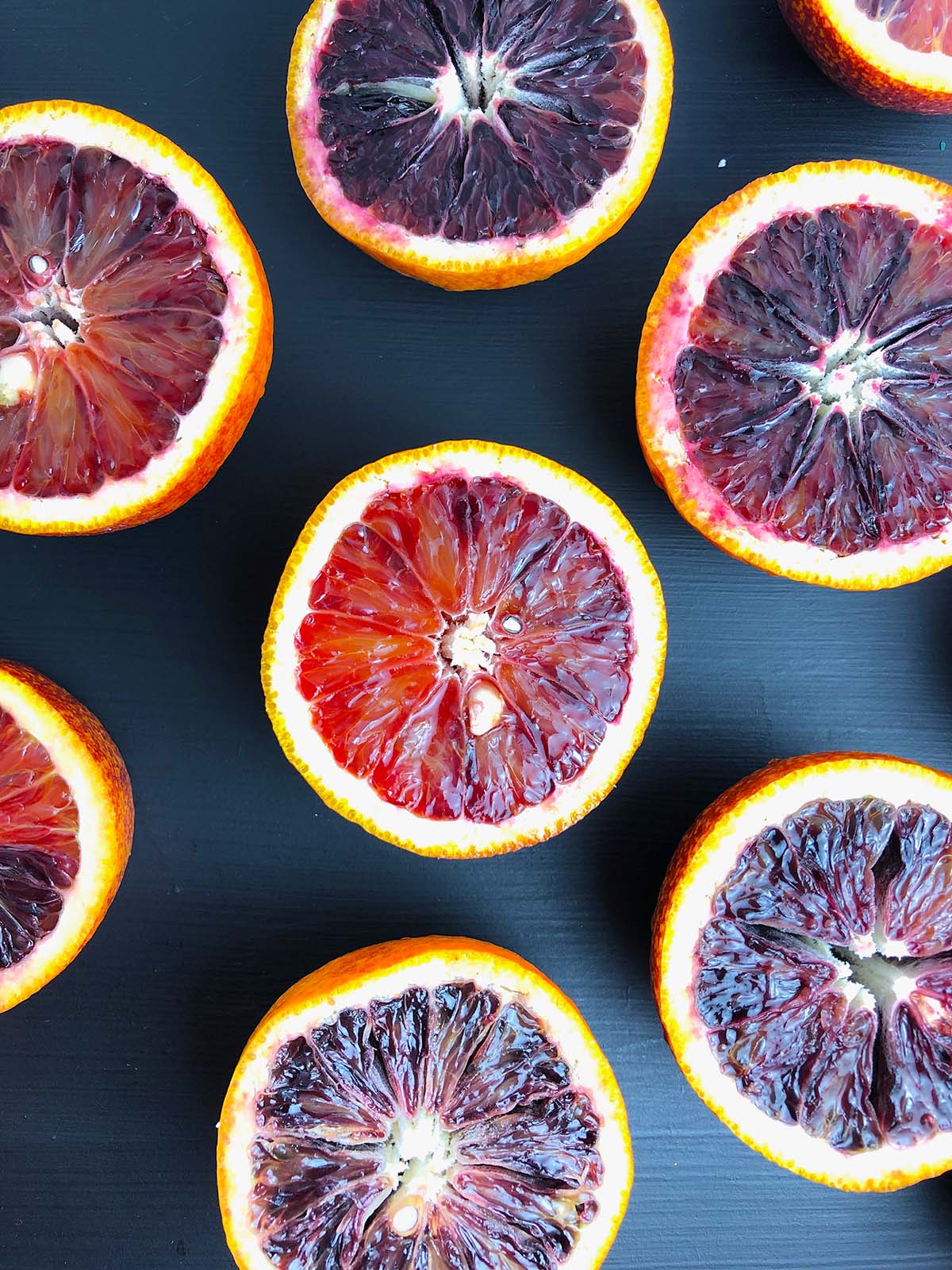 cut halves of blood oranges against a black background