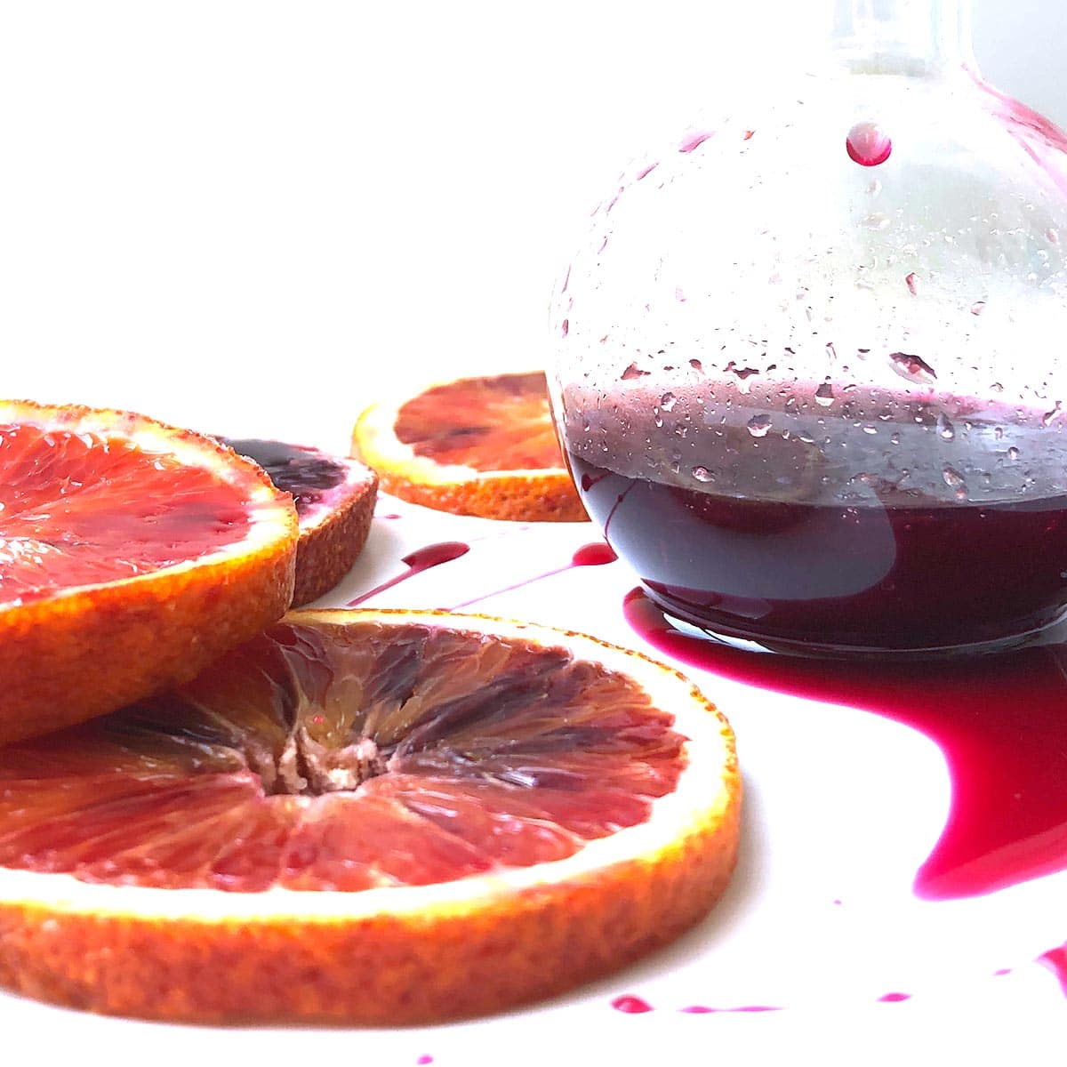 Beaker jar with blood orange syrup, surrounded by sliced blood oranges