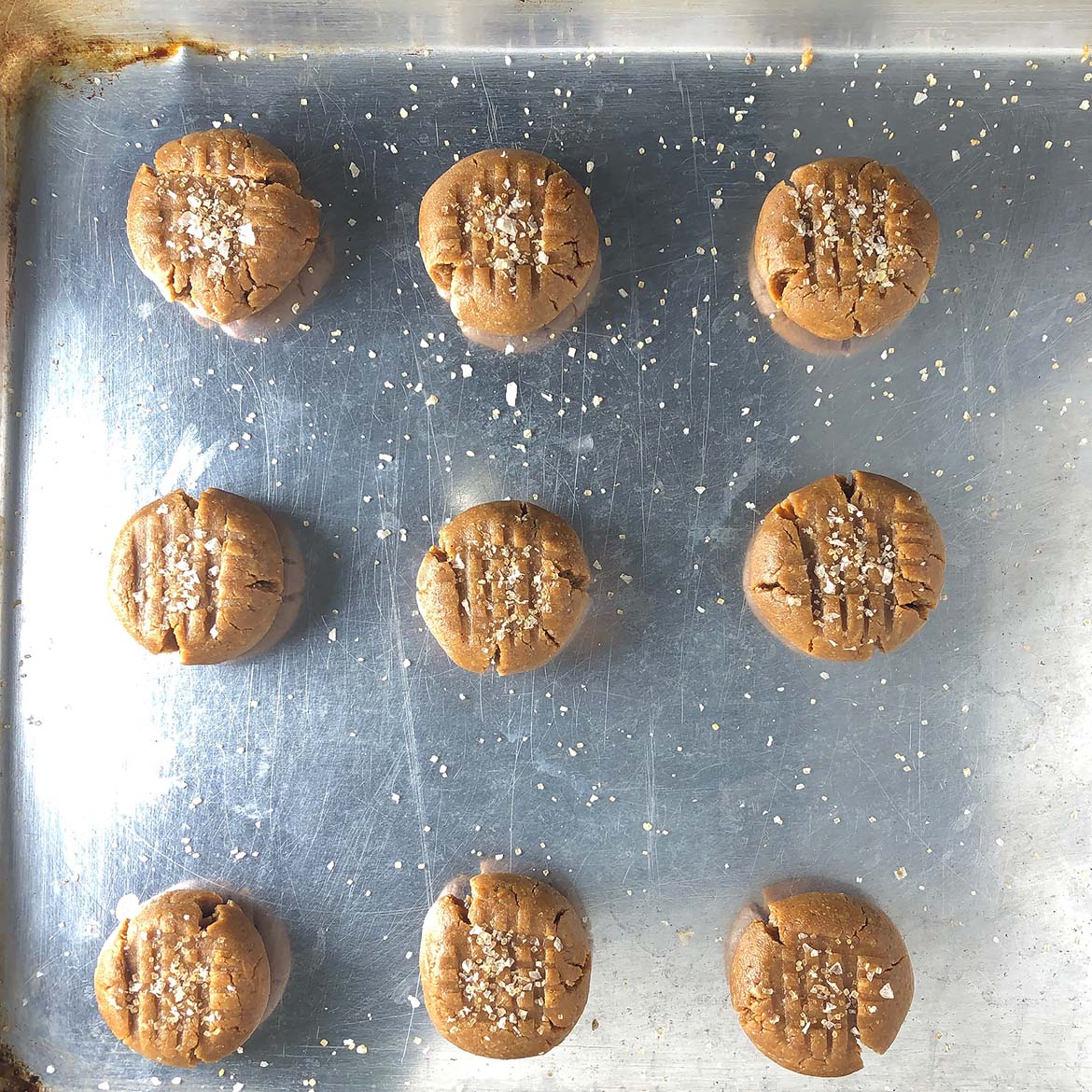 Top-down view of Peanut Butter Cookies on baking sheet, sprinkled with salt and sugar topping.