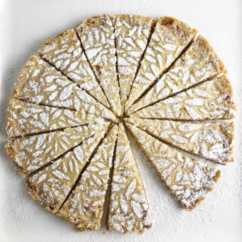 Top-down shot of triangles of Vegan Brown Butter Shortbread on a white plate. Shortbread is decorated with lemon-infused sugar.