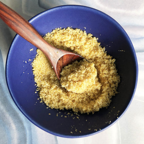 Top-down close up view of 1-Minute Plant-Based Parmesan Cheese, in a blue bowl with a small wooden spoon