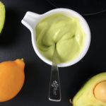 Top-down view of Lemony Avocado Caesar Dressing in a white picture. Dressing is light green and creamy, and is being stirred with a spoon.