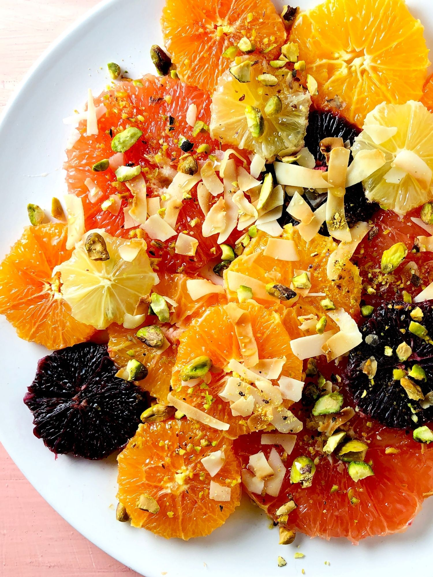 Top down view of Simple Citrus Salad with text Get Some Sun, and a top down shot of the salad – slices of pink grapefruit, navel oranges, tangelos, blood oranges, and lemon, garnished with ribbons of toasted coconut, crushed pistachios and honey.