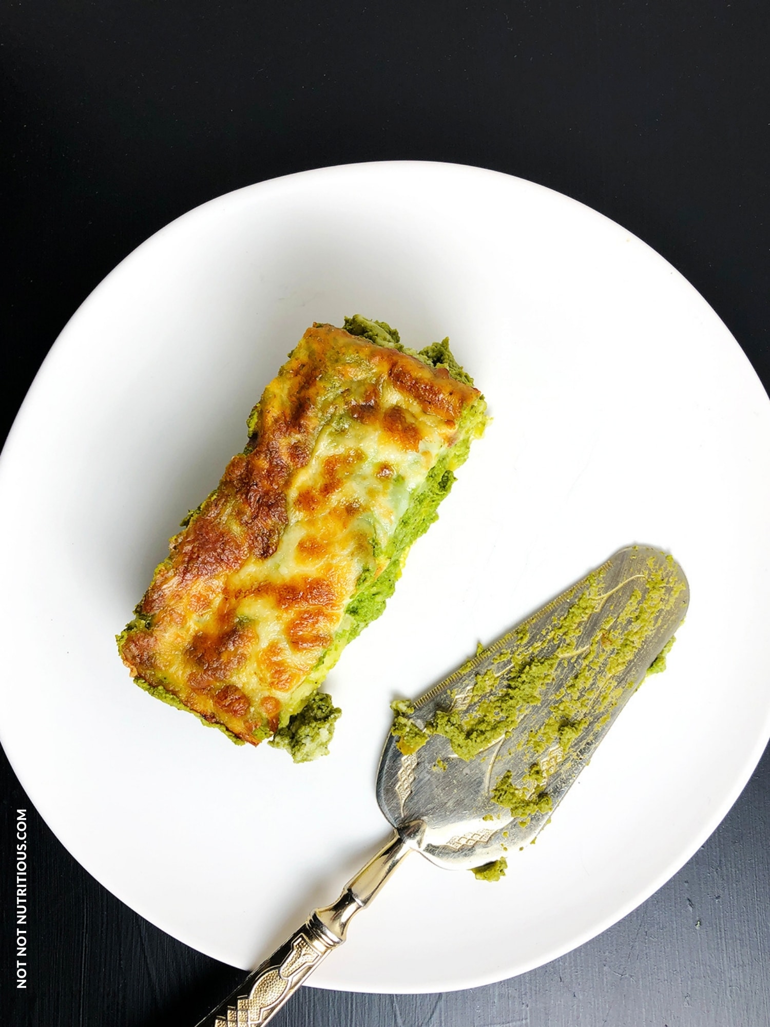 Top-down shot of slice of green lasagna on a white plate. A serving utensil sits next to the lasagna on the same plate.