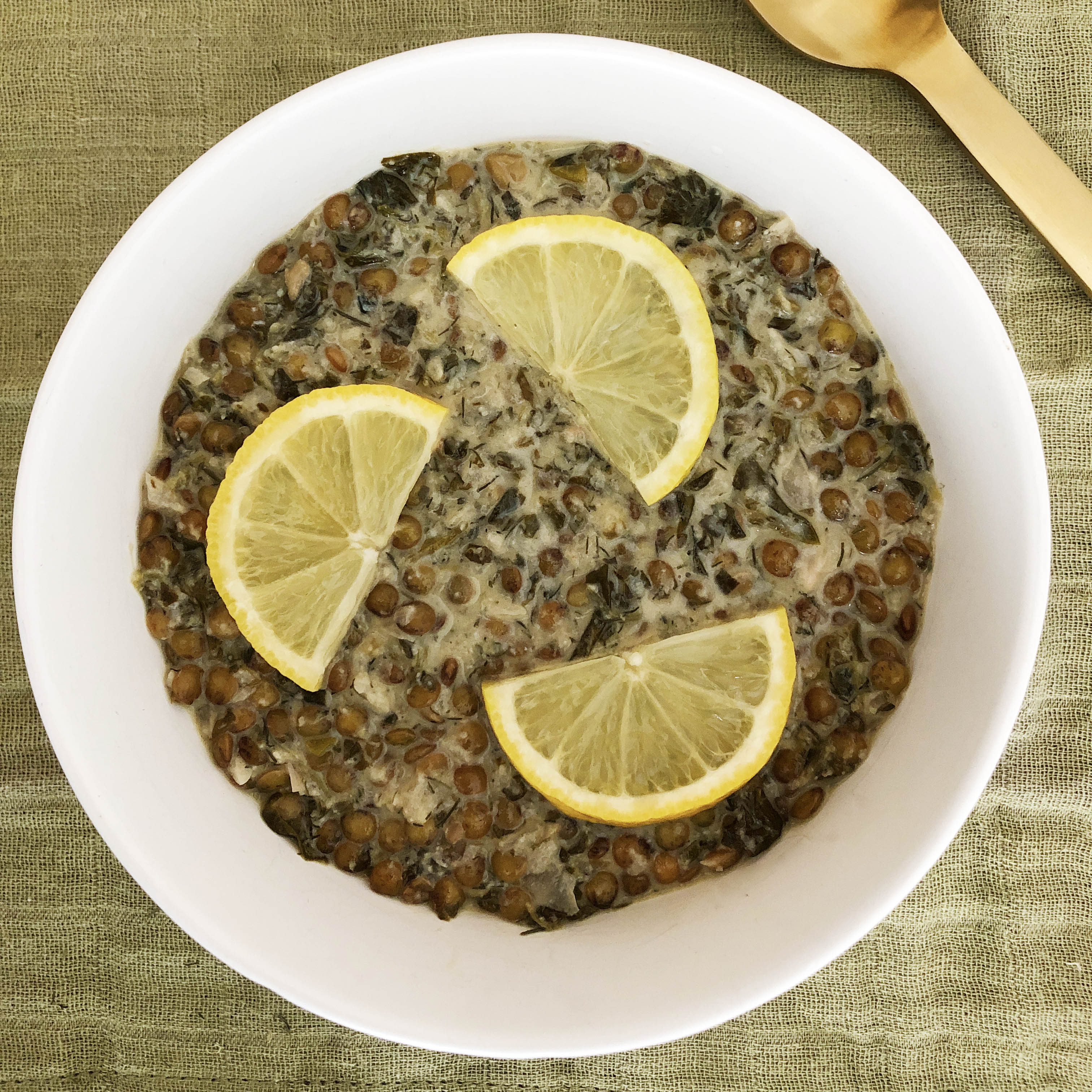 Top-down view of white bowl with lentil lemon and dill soup, topped with lemon slices