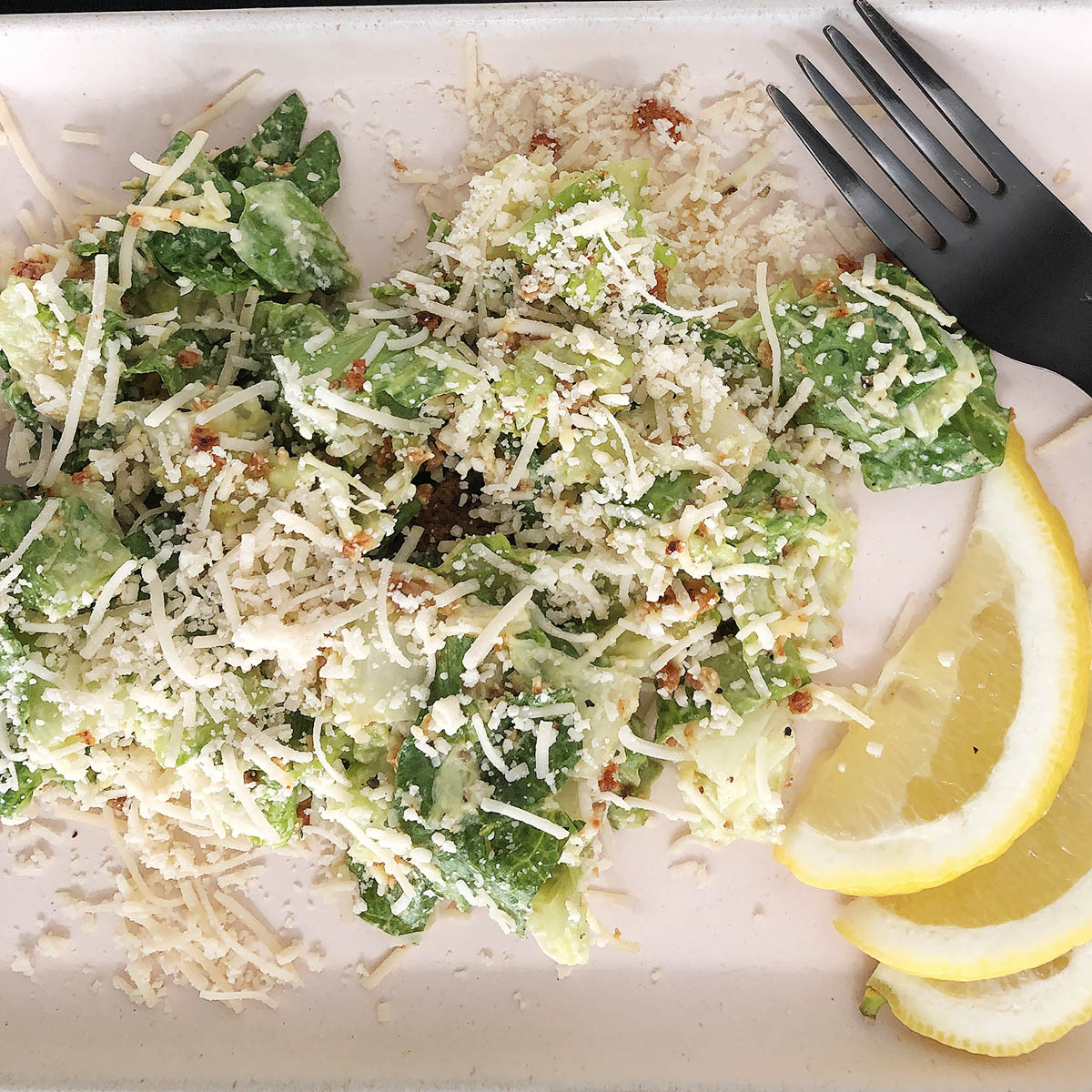 Top-down view of Plant-based Caesar Salad in a black bowl. Salad is garnished with lemon slices.
