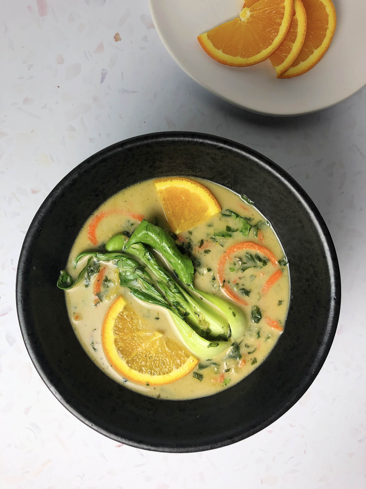 Top-down shot of Thai Green Curry in a black bowl, garnished with bok choy and oranges slices