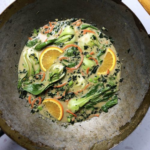 Top-down shot of Thai Green Curry in an old wok, with baby bok choy, carrots, spinach, and edamame beans.