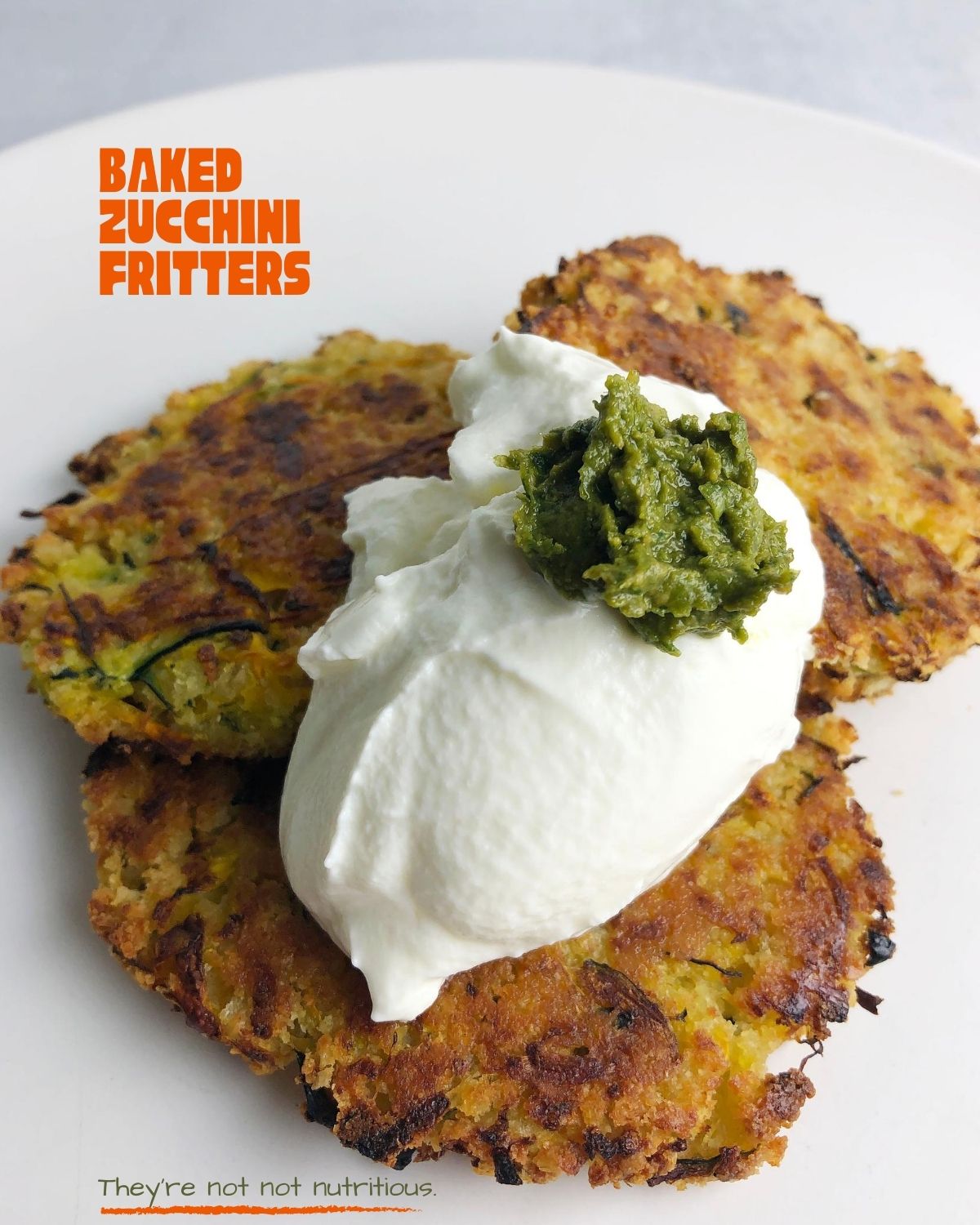 Side view of three Baked Zucchini Fritters topped with sour cream and pesto