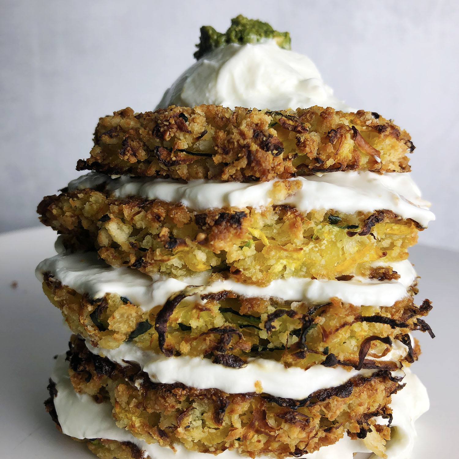 Stack of Baked Zucchini Fritters layered with plain yogurt and topped with yogurt and pesto.