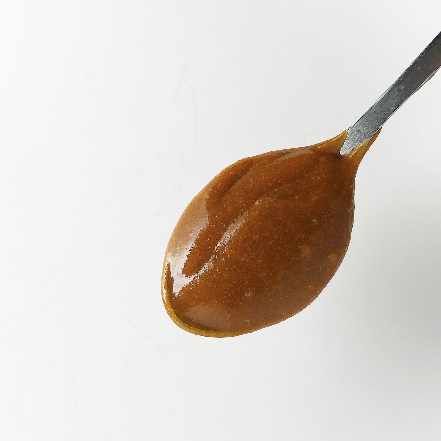 Top-down shot of spoon with brown butter barbecue sauce against a white background