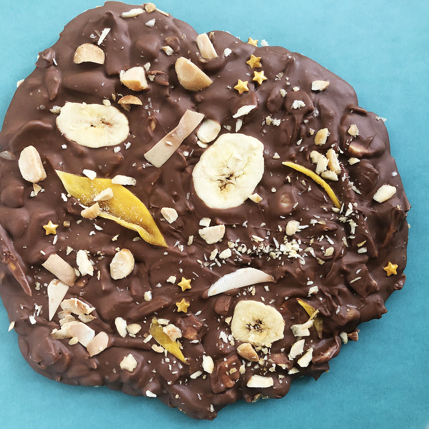Top-down view of Milk Chocolate Bark with tropical ingredients: dried mango, banana chips, toasted coconut, and macadamia nuts