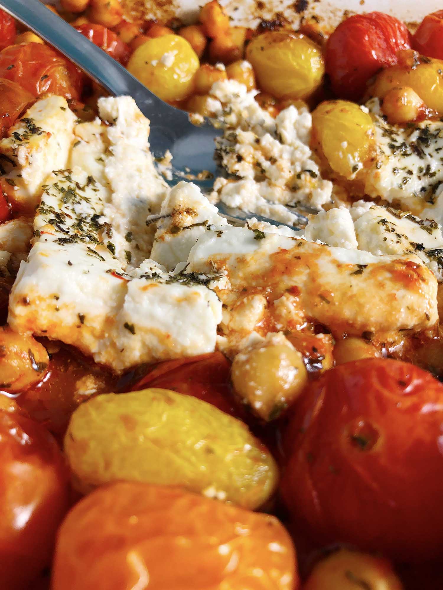 Close up of for, mashing the baked feta into the Chickpea Feta Bake