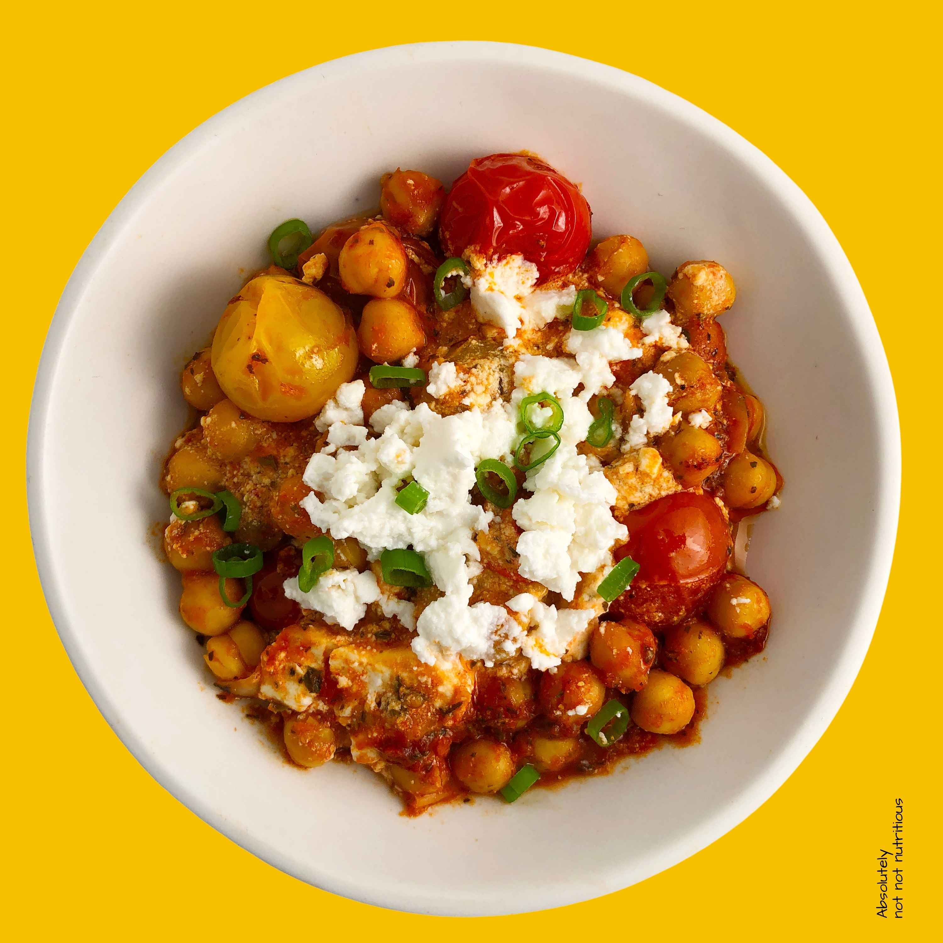 Top-down view of Chickpea Feta Bake in a white bowl. Topped with extra feta and green onions.