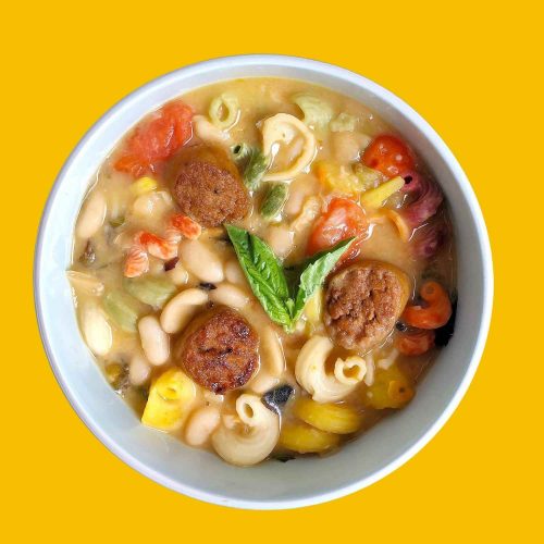 Top-down view of bowl of Garlicky White Bean Soup, made with leafy greens, sweet tomatoes, and spicy plant-based sausage.