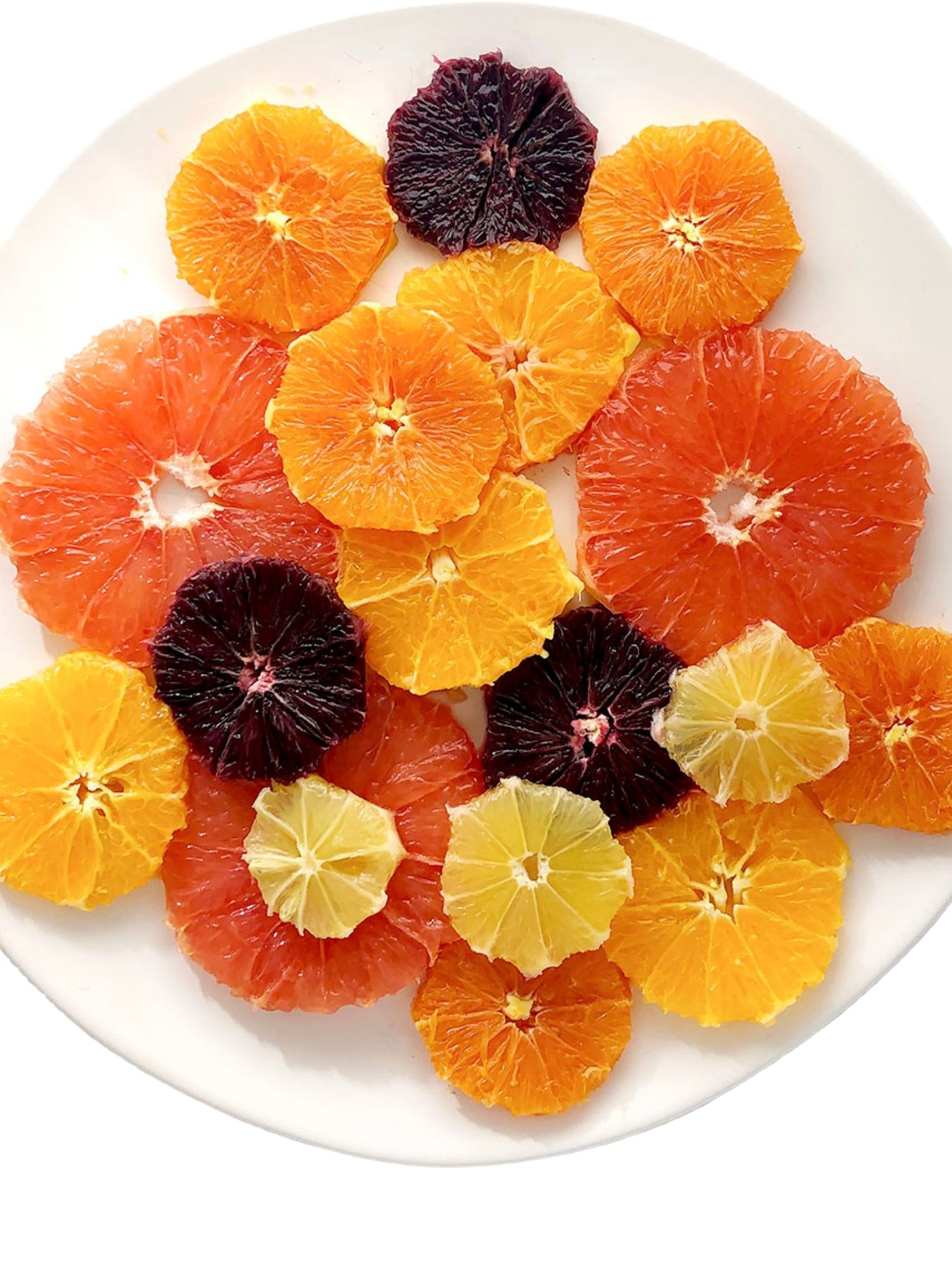 Top down shot of white plate with slices of pink grapefruit, navel oranges, tangelos, blood oranges, and lemon. This is one of the steps in making Simple Citrus Salad.