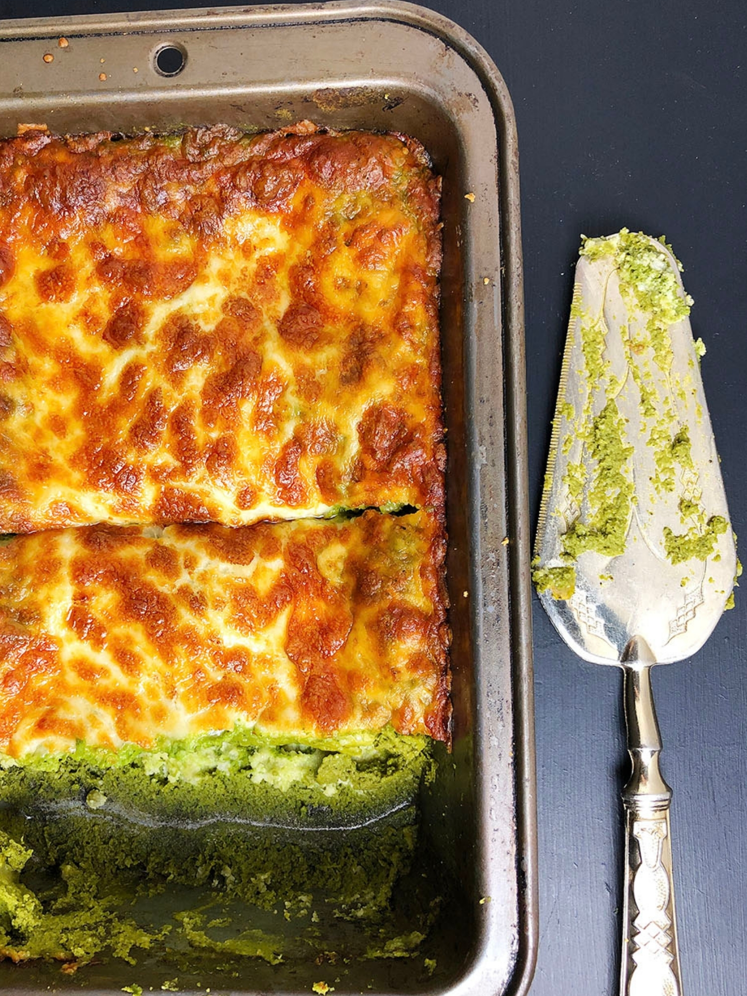 Top-down shot of green lasagna in a baking dish, with a slice of lasagna removed from the dish. 