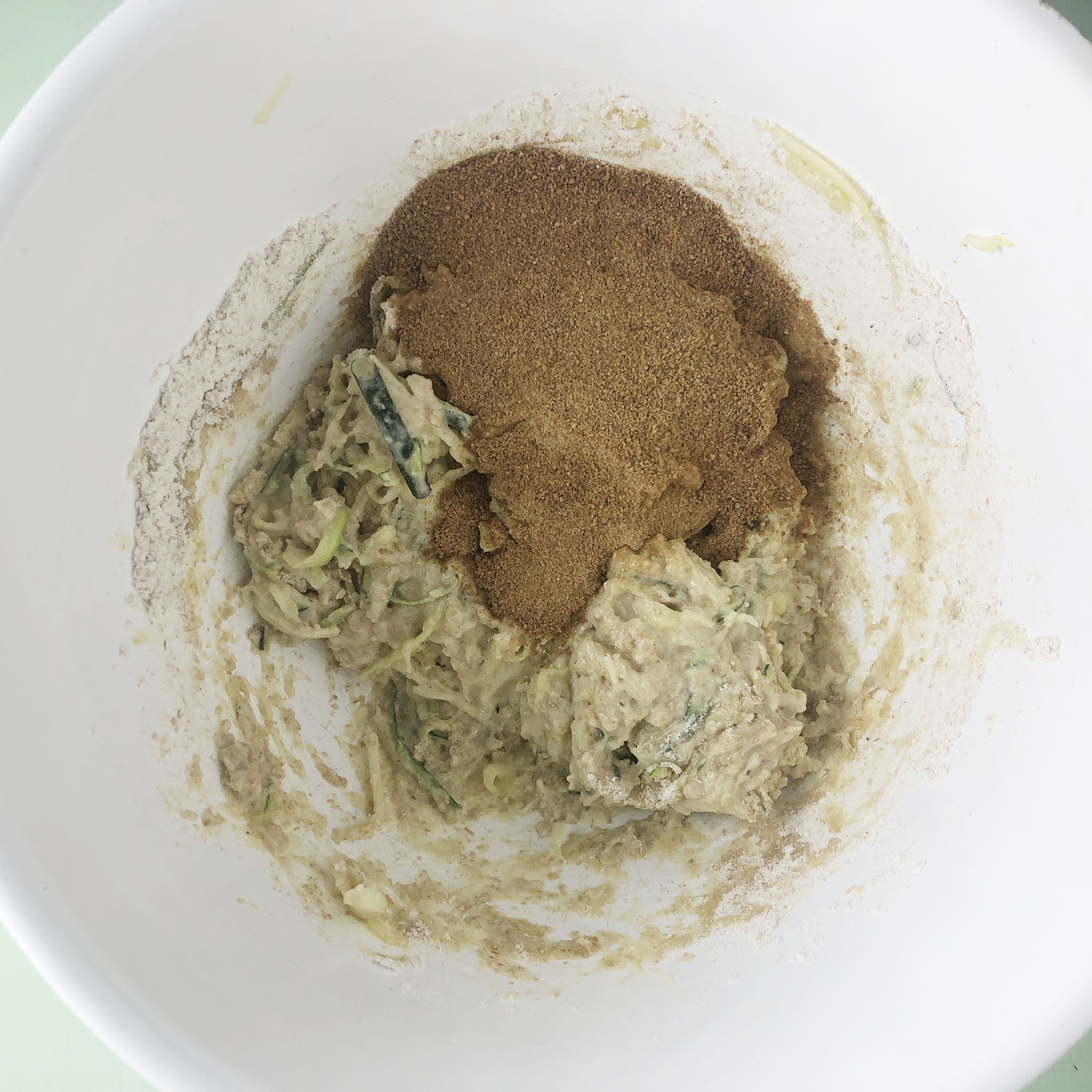 Top-down of white bowl with coconut sugar and hemp seeds, plus other ingredients for muffins.