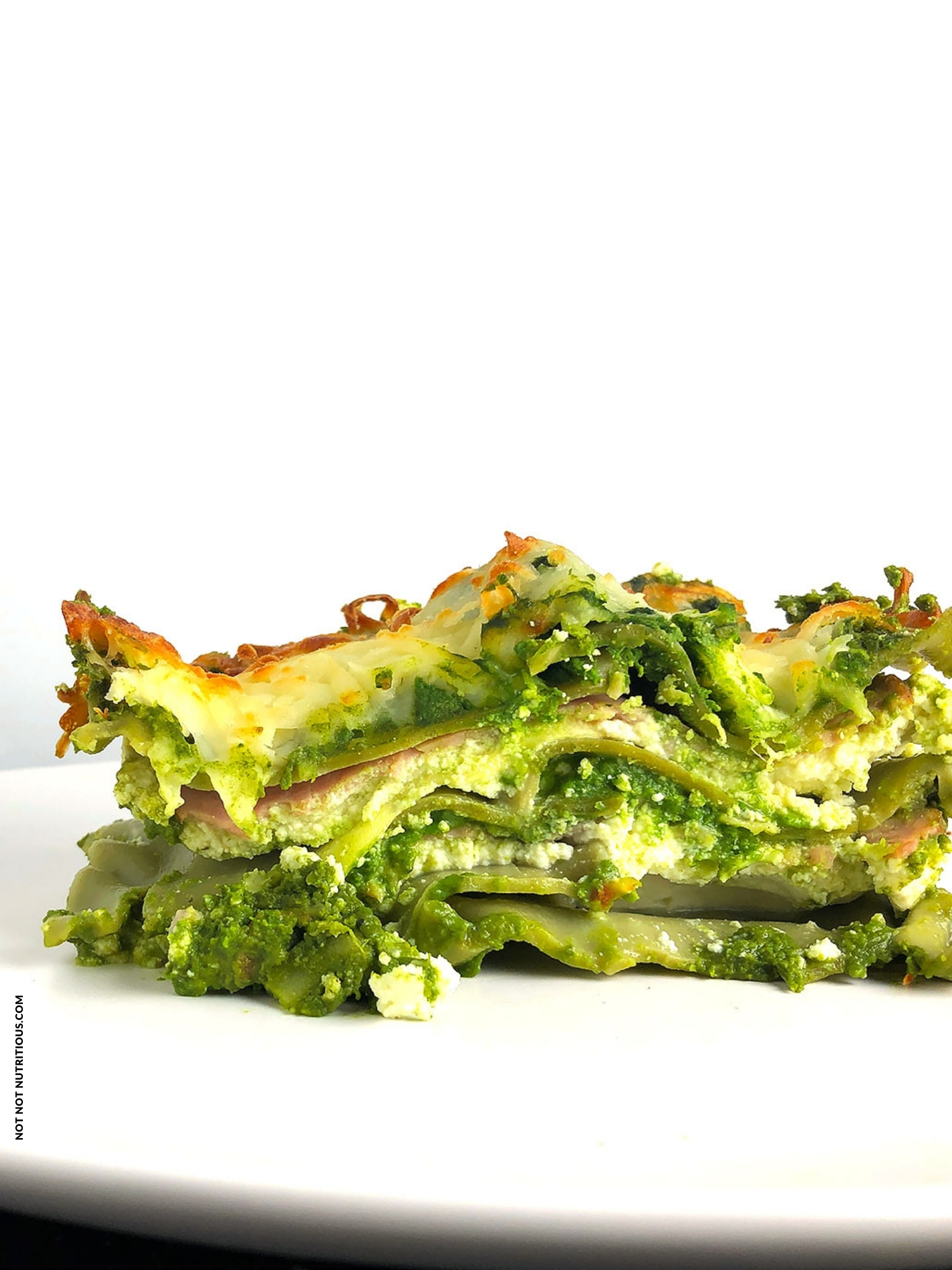 Side shot of slice of Green Lasagna on a black plate against a white background. 