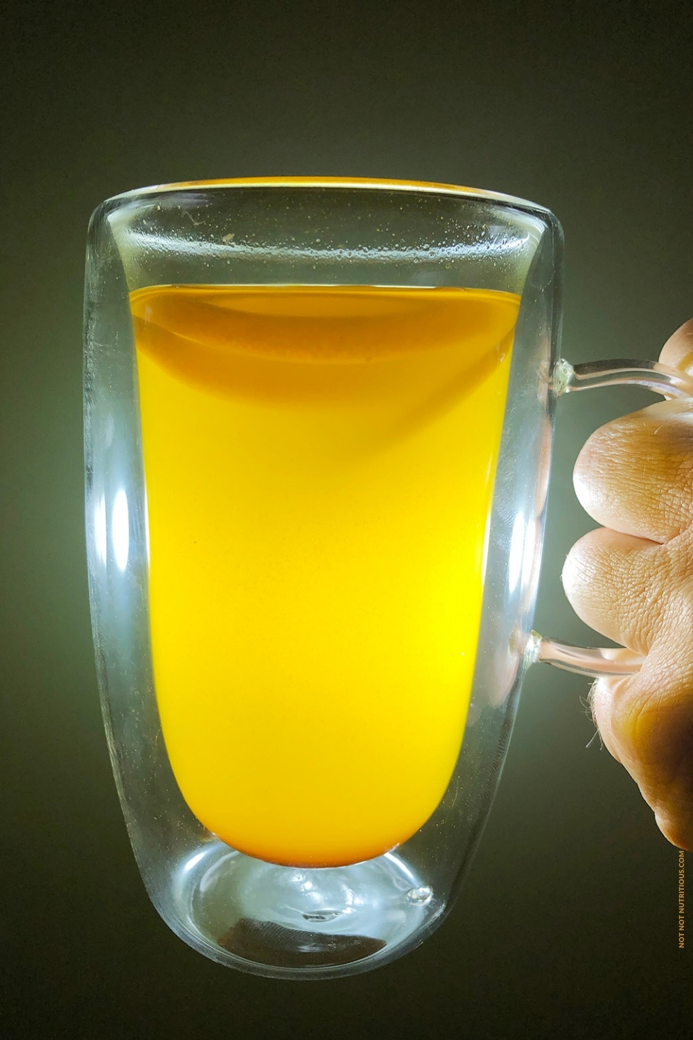 Side view of man's hand holding a clear mug with hot lemonade.