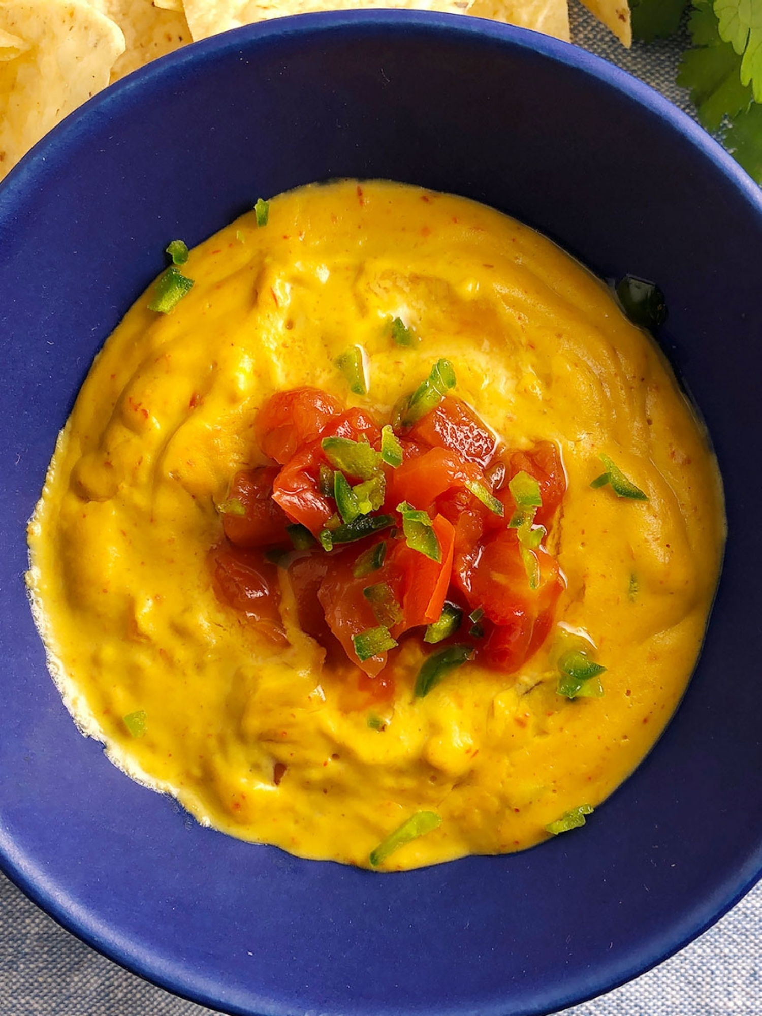Top-down of easy vegan queso topped with chopped tomato, in a bright blue bowl