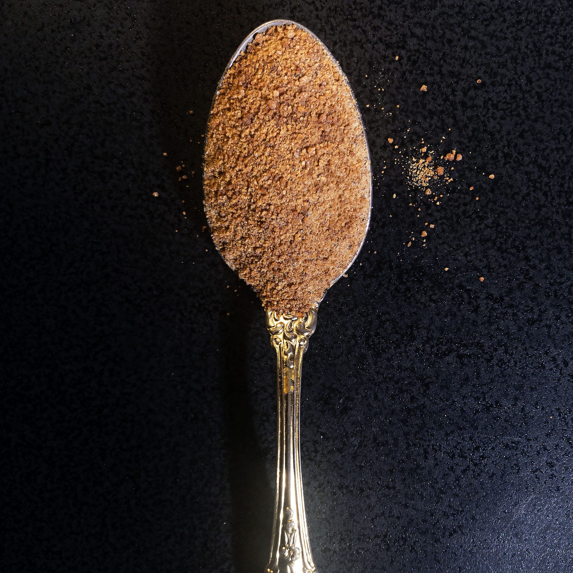 Coconut sugar on a spoon, against a black background