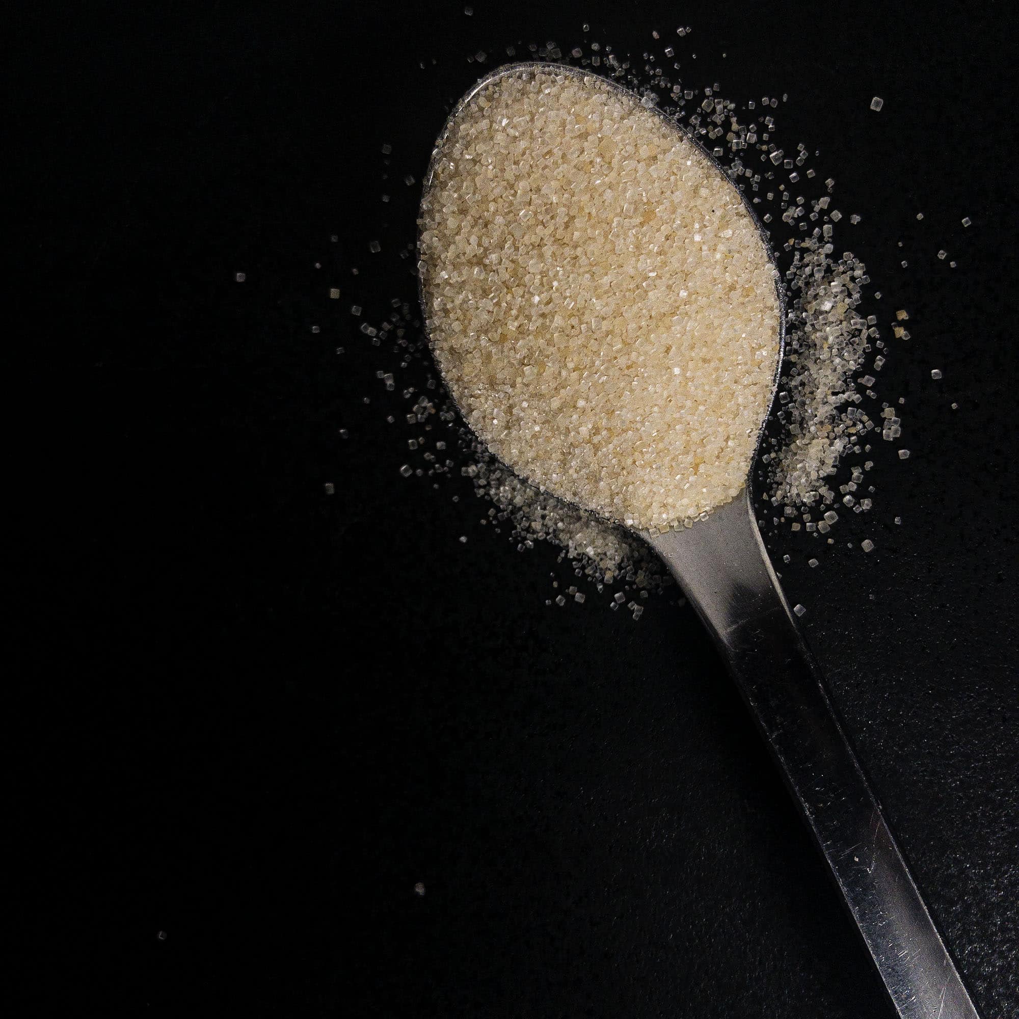 cane sugar on a spoon, against a black background
