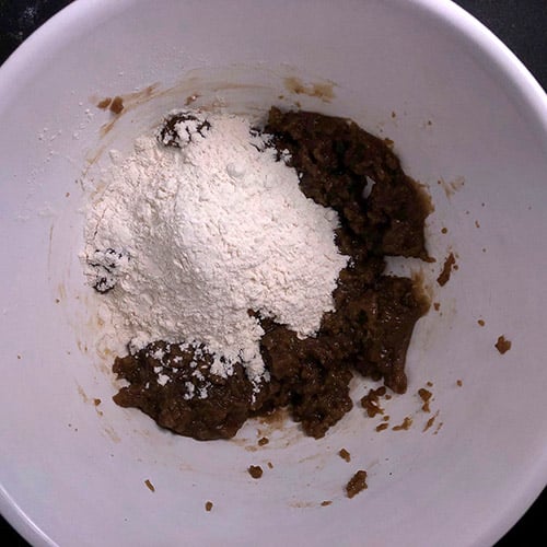 Top-down view of white mixing bowl with flour, salt, and cornstarch added to sugar, butter and vanilla