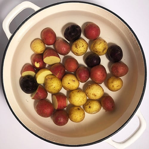 Top-down view of baby potatoes in large white pot, covered with water